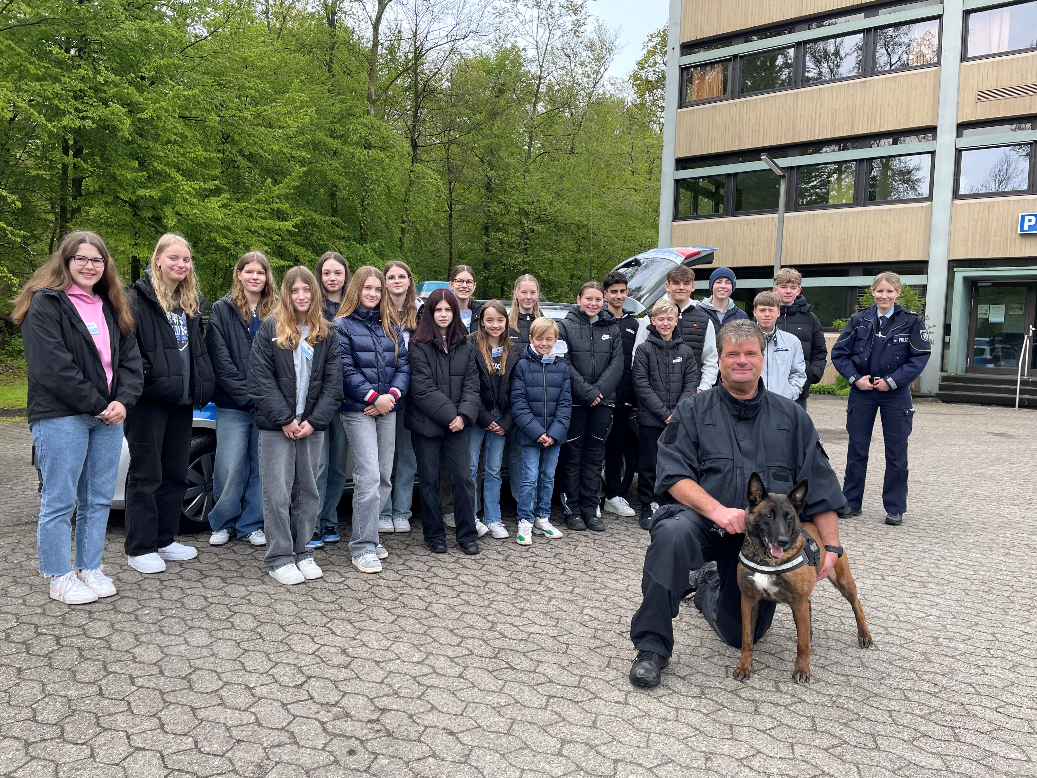 Gruppenfoto Berufsfelderkundungstag mit Diensthundführer Dirk Patzke im Vordergrund. Das Foto wurde in der Waldstraße 20 in Detmold vor dem Polizeigebäude angefertigt.