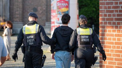 Ein 14-jähriger Junge wird von einem Polizisten und einer Polizistin in der Düsseldorfer Altstadt abgeführt. Im Hintergrund ist eine Kirche zu sahen. 