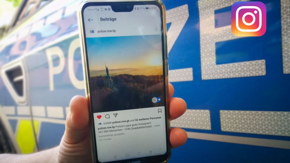 Smartphone mit dem Instagram-Profil der Polizei Lippe vor dem Hintergrund eines Streifenwagens