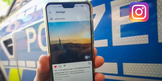 Smartphone mit dem Instagram-Profil der Polizei Lippe vor dem Hintergrund eines Streifenwagens